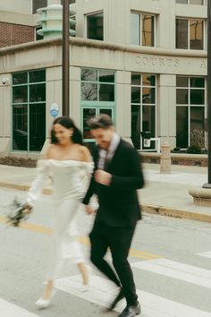 a bride and groom crossing the street in front of a building