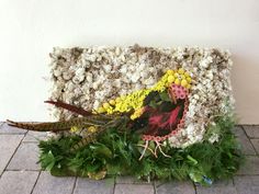 a piece of art made out of flowers and feathers on a brick floor next to a wall