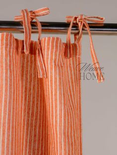 an orange and white striped curtain hanging from a metal rod with two ties on it