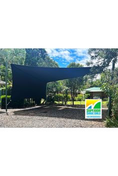 a large black shade structure in the middle of a gravel area with trees and bushes around it