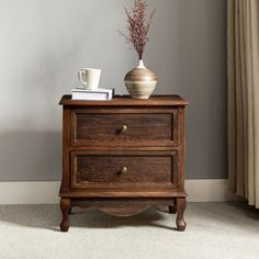 a small wooden cabinet with two drawers and a vase on top, in front of a window