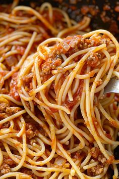 spaghetti being cooked in a skillet with a ladle full of sauce and meat