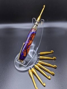 a gold and purple pen sitting on top of a glass holder with six golden screwdrivers