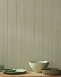 bowls and plates are sitting on a wooden table in front of a wall with vertical stripes