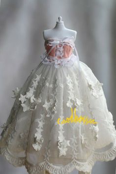 a white dress with flowers and lace on the skirt is sitting on a mannequin