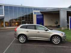 a silver volvo car is parked in front of a building with glass windows and grass