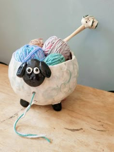 a ceramic sheep with yarn in it's mouth sitting on a table next to a wall