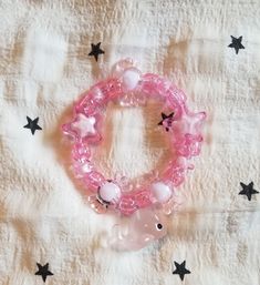 a pink beaded bracelet with an elephant and stars on the fabric behind it is laying on top of a white sheet