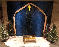 a nativity scene with a crib and christmas trees in front of a backdrop