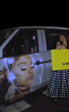 a woman holding up a yellow sign in front of a car that is advertising selfridge