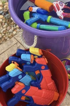 two buckets filled with plastic toys on top of a stone floor next to rocks