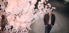 a man is walking down the street in front of some pink flowers with his eyes closed