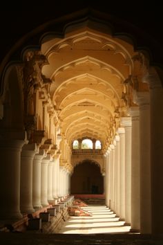 the inside of an old building with columns and arches on both sides, looking down at rows of empty benches