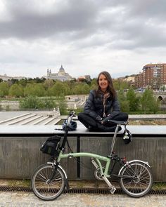 a woman sitting on top of a bridge next to a green bike with the city in the background