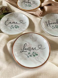 three plates with names on them sitting on a cloth covered tablecloth next to flowers