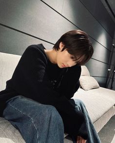 a young man sitting on top of a couch next to a white pillow in a room