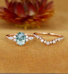 two rings sitting on top of a table with flowers in the background and one has a green stone