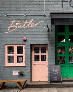 the outside of a restaurant with green doors and pink windows, along with a wooden bench in front of it