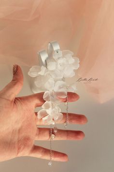 a person's hand holding a white flower and chain