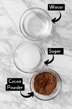 three bowls with ingredients labeled on them sitting on a marble counter top, including sugar, cocoa powder and water