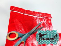 a pair of scissors sitting on top of a red tie - dyed piece of cloth