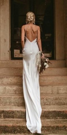 the back of a woman in a white dress standing on some steps with her bouquet