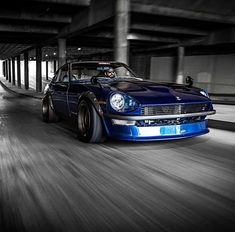 a blue car driving down a street next to a parking garage with lots of lights