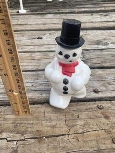 a snowman figurine sitting on top of a wooden floor next to a ruler