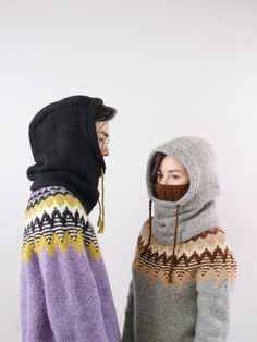 two people standing next to each other wearing sweaters and hoodies with their faces covered