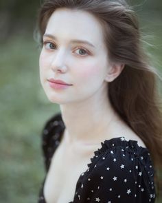 a woman with long brown hair wearing a black and white top is looking at the camera