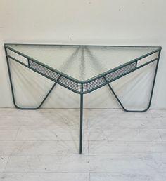 a glass table with metal frame and mesh top on the floor in front of a white wall