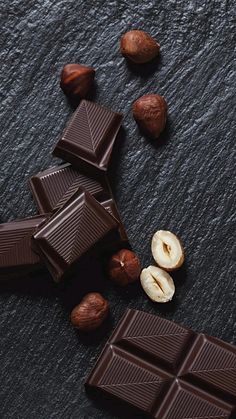 chocolate and nuts on a black surface with one broken in half, the other unwrapped