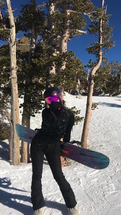 a snowboarder is holding her board while standing in the snow near some trees