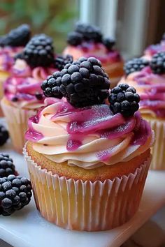 some cupcakes with frosting and blackberries are on a white platter