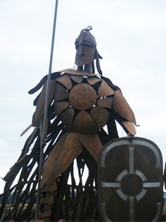 a statue made out of wood with a man standing on it's shoulders and holding a shield