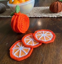 three crocheted oranges sitting on top of a wooden table next to a bowl of oranges