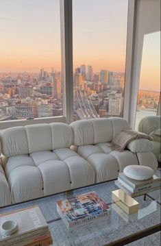 a white couch sitting in front of a window next to a table with books on it