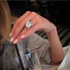 a woman is sitting at a table with a glass and a ring on her finger