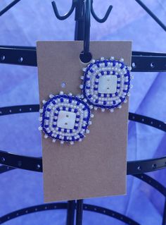 a pair of blue and white beaded earrings hanging from a metal hook on a piece of cardboard