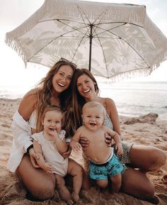 three women and two babies on the beach under an umbrella