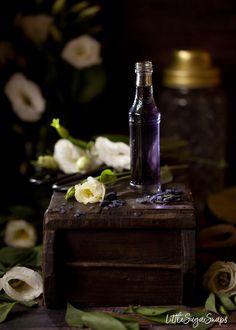 an empty bottle sitting on top of a wooden box next to white flowers and greenery