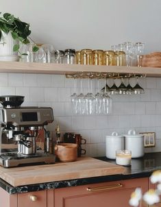 a kitchen counter topped with lots of glasses and coffee maker next to a shelf filled with cups