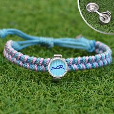 a blue and pink braided bracelet with an anchor charm on it, sitting in the grass