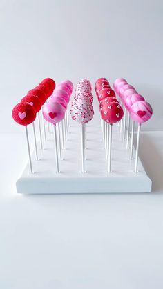 six heart shaped lollipops are lined up on a white stand with pink and red sprinkles