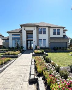 a large white house with lots of flowers in the front yard and walkway leading to it