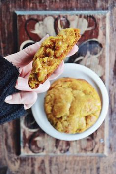 a person holding a piece of food in front of a muffin on a plate