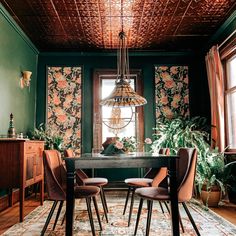 a dining room with green walls and floral wallpaper on the ceiling, along with wooden chairs