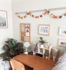 a bedroom with a desk, chair and pictures on the wall above it is also decorated with potted plants