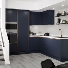 a kitchen with dark blue cabinets and white counter tops, stairs leading up to the upper floor