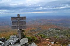 a wooden sign on top of a mountain with lots of trees in the back ground